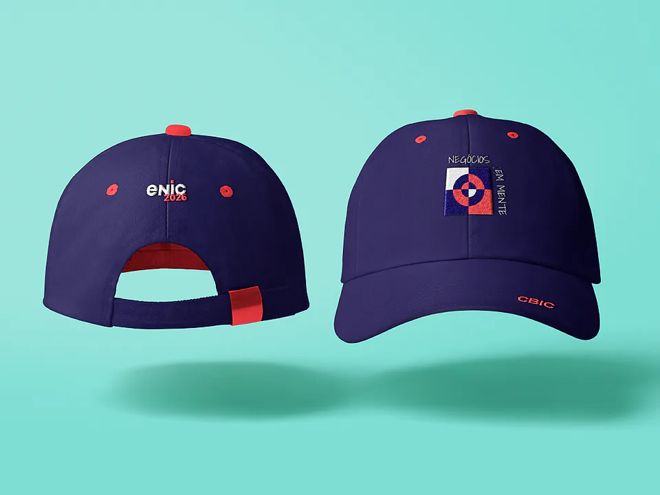 Dois bonés azul-marinho, um com a marca ENIC 2026 e outro com o símbolo em vermelho e branco, sobre fundo turquesa