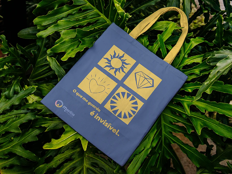 Tote bag azul com quatro ícones amarelos e a frase o que me governa é invisível