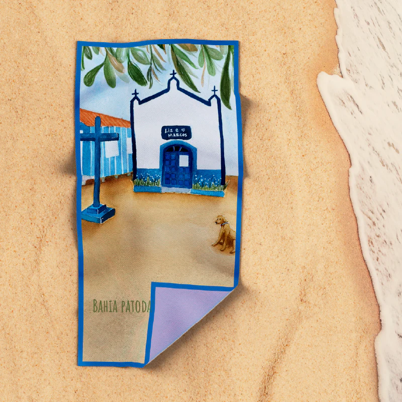 Toalha de praia com a capela azul ilustrada, estendida sobre a areia
