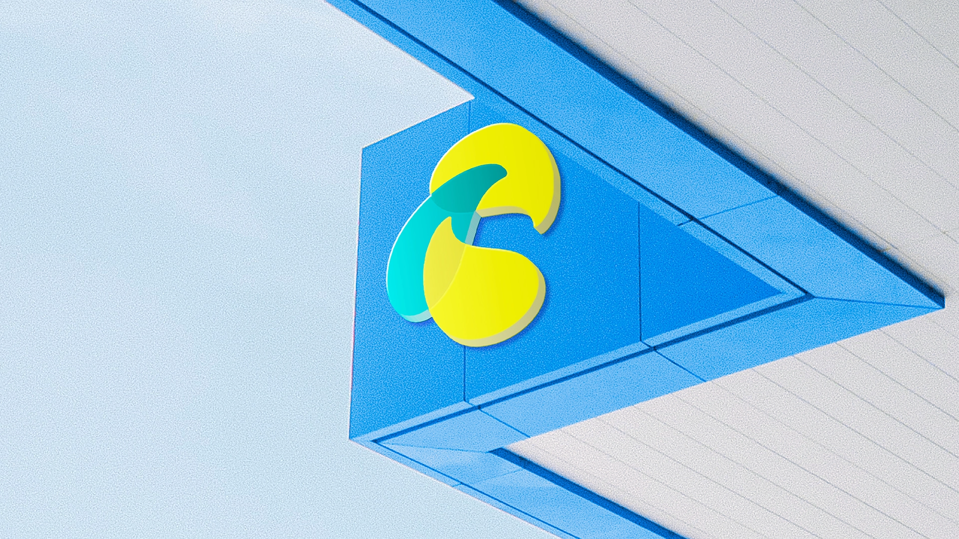 Símbolo da Evlo em verde e amarelo aplicado em alto-relevo na quina de uma estrutura arquitetônica azul, contra céu claro ao fundo.